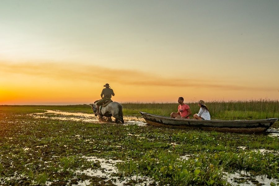 Jinete a caballo y pareja en canoa en los Esteros del Iberá al atardecer